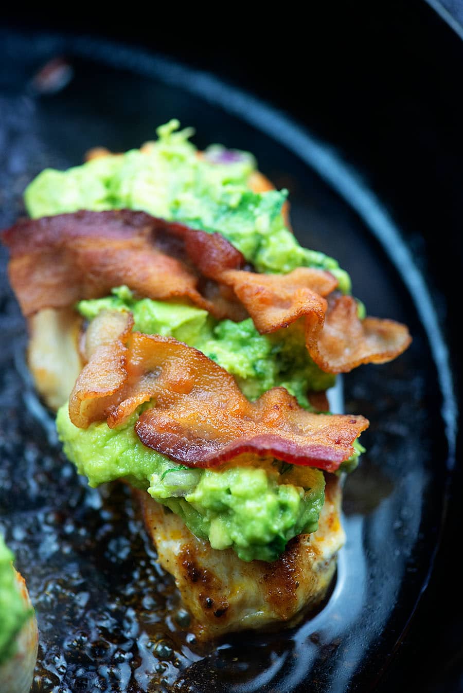 chicken frying in a cast iron skillet topped with guacamole and bacon