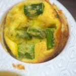 quiche in a white muffin pan with pieces of asparagus and ham