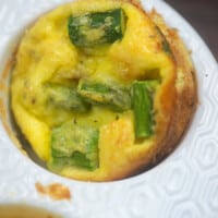 quiche in a white muffin pan with pieces of asparagus and ham