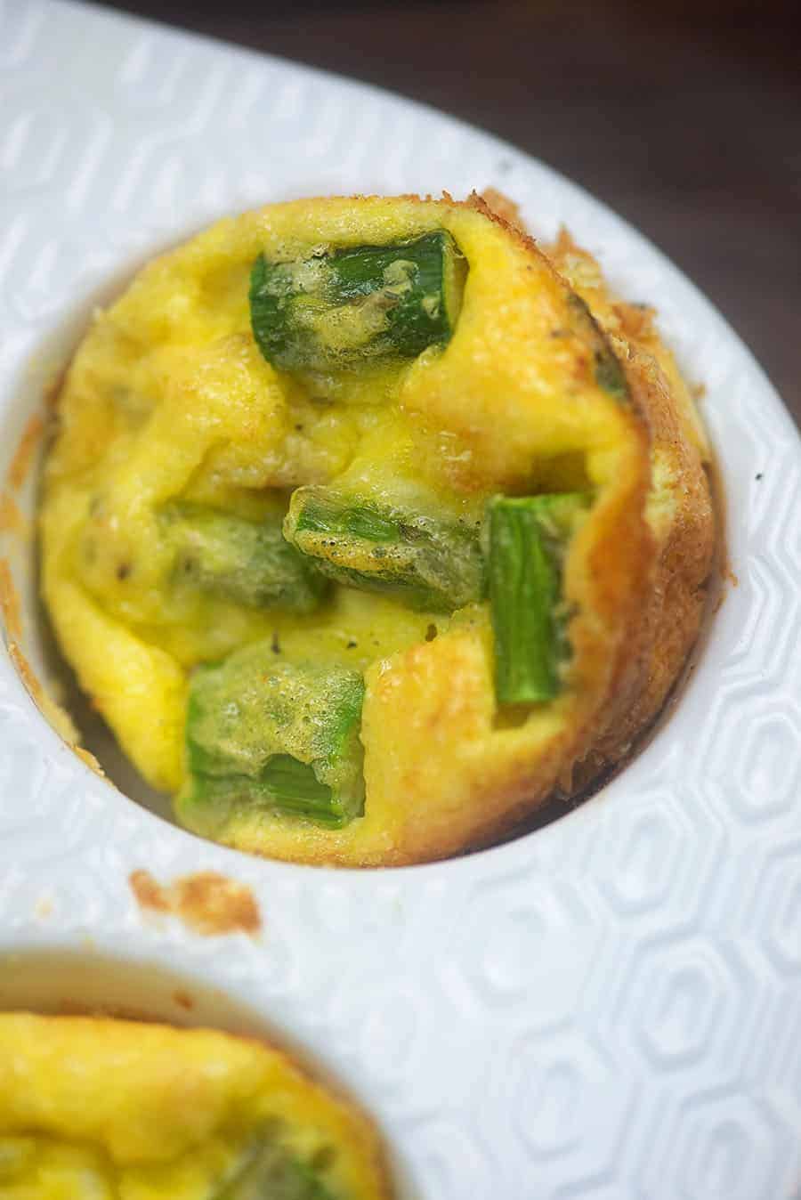 quiche in a white muffin pan with pieces of asparagus and ham