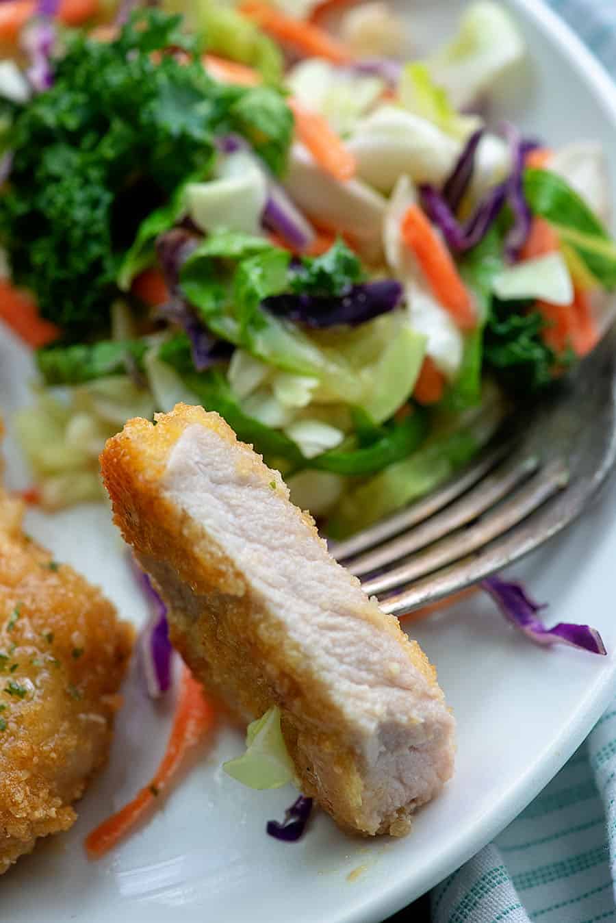 A bite of pork shop on a fork resting on a white plate