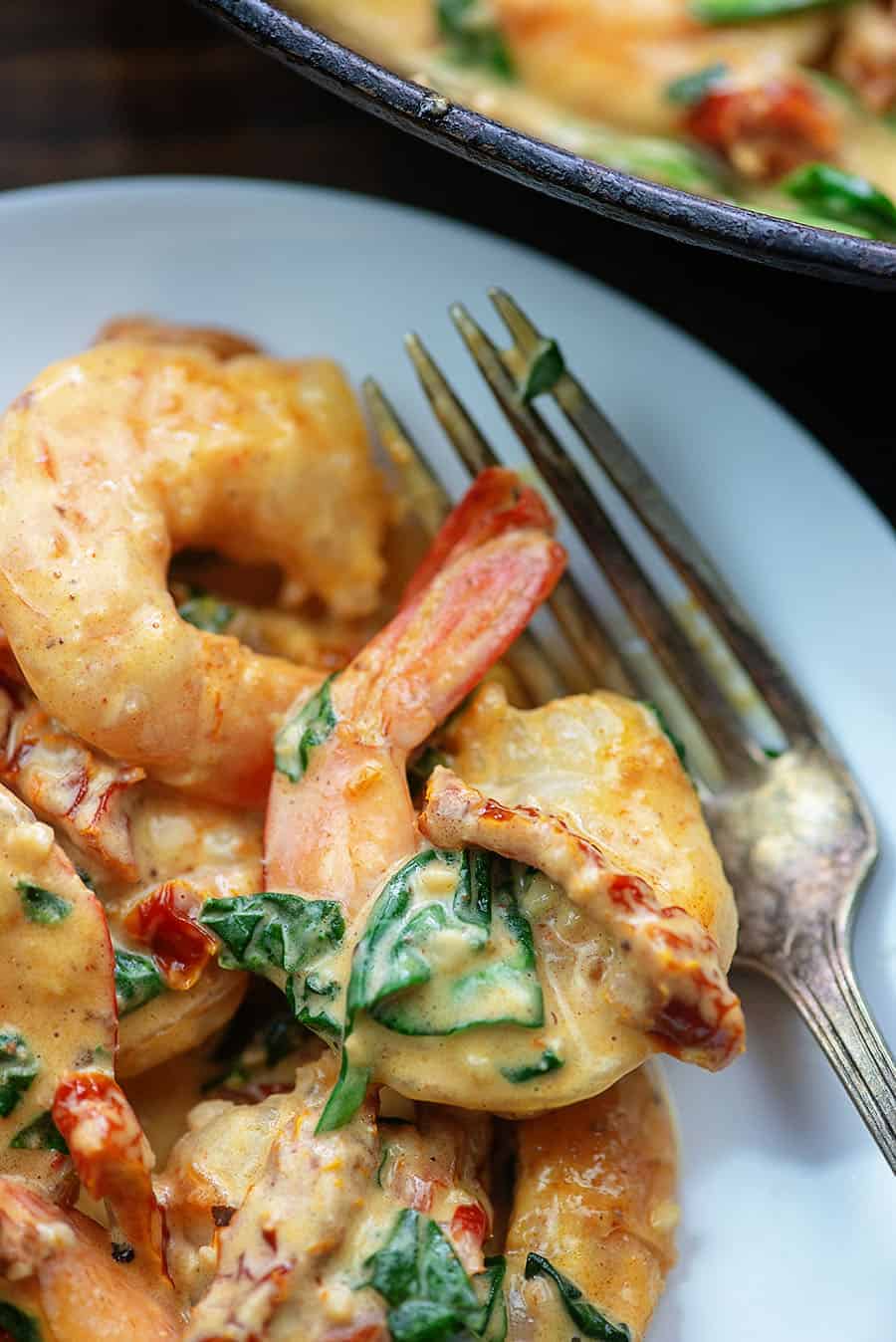 A close up of Tuscan shrimp on a white plate next to a fork.