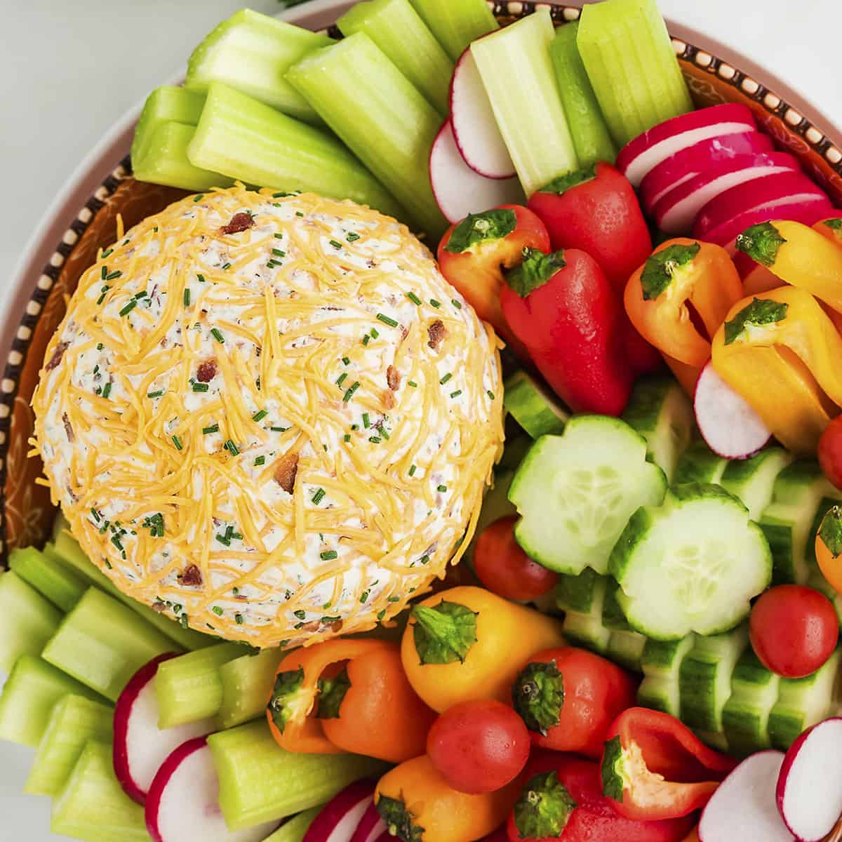 Cheese ball on platter surrounded by celery, cucumbers, and more low carb vegetables.