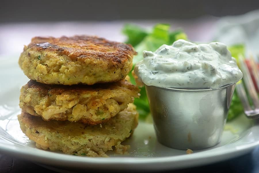 A close up of stacked salmon patties on a plate next to a cup of dip.