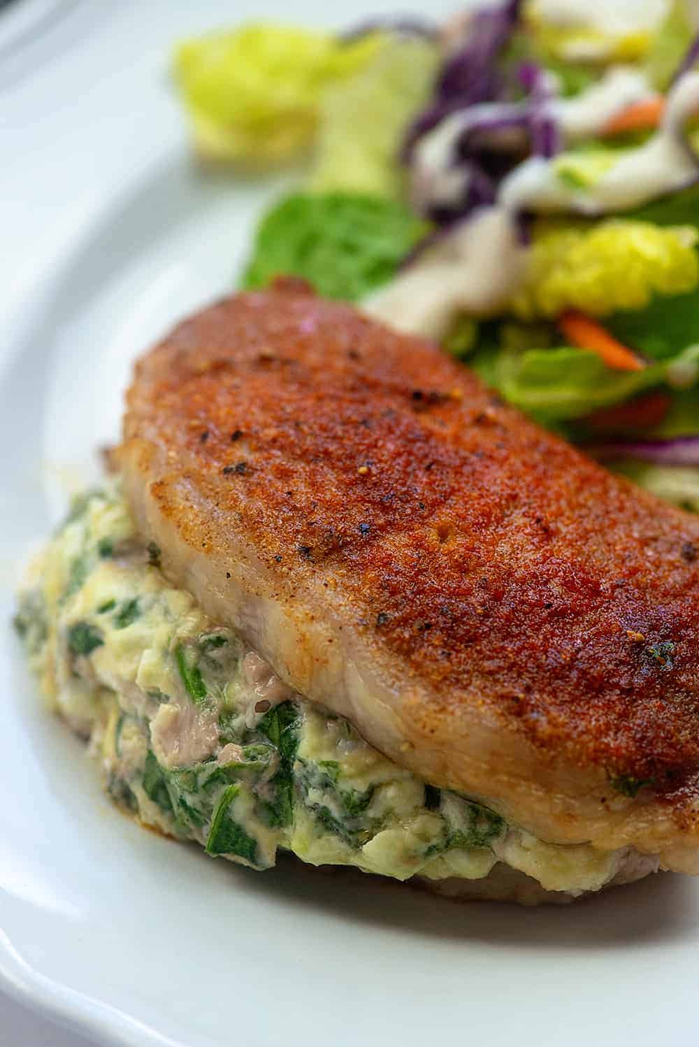 A close up of a stuffed pork chop on a white plate.