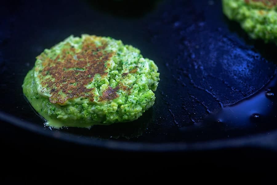 A close up of a broccoli fritter cooking on a skillet.