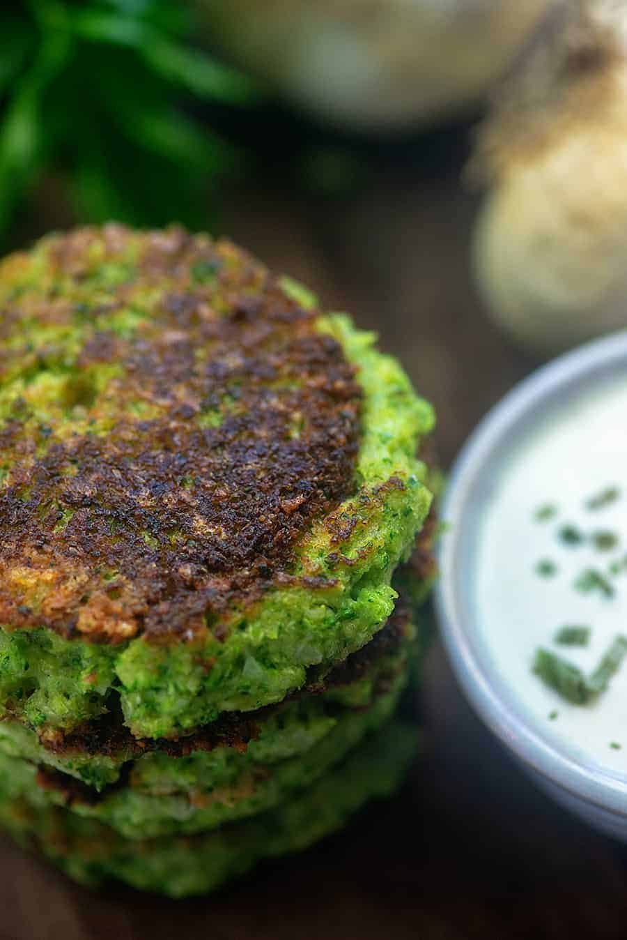 A stack of broccoli fritters next to a bowl of dip.