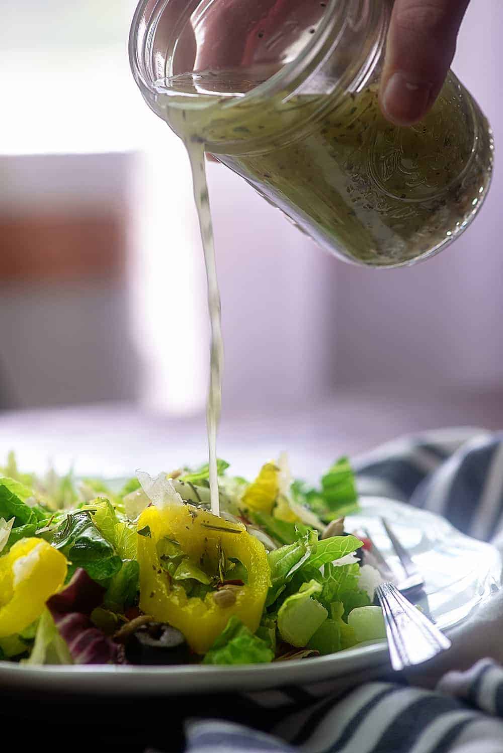 homemade Italian dressing being poured out of a jar onto a salad