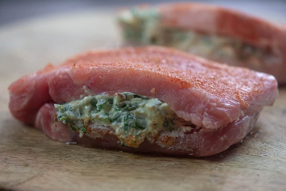 Raw spinach stuffed pork chops on a wooden cutting board.