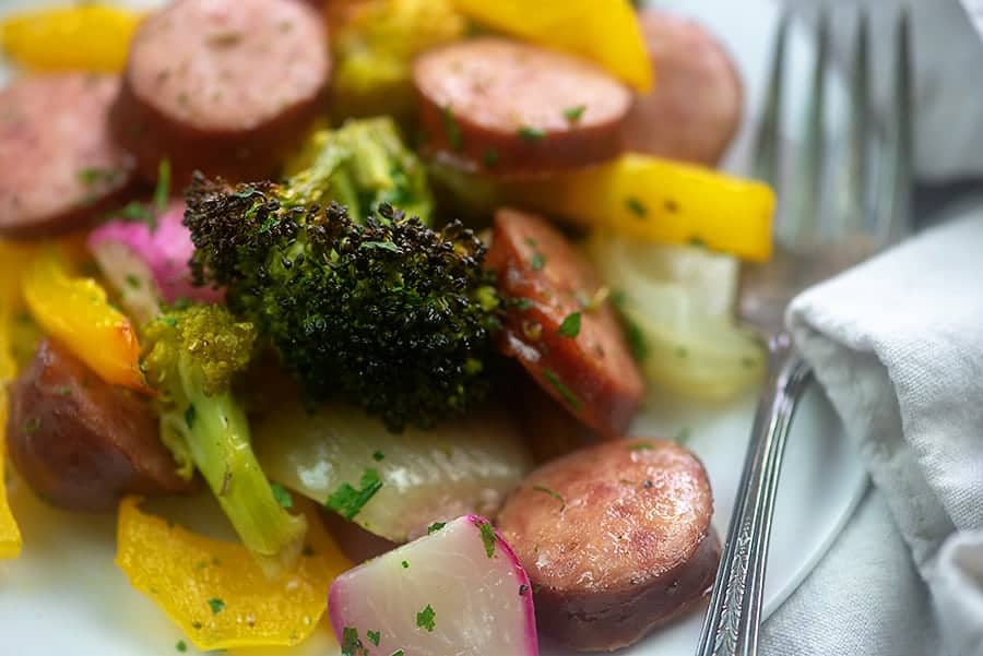 A plate of various vegetables and sausage with a fork.