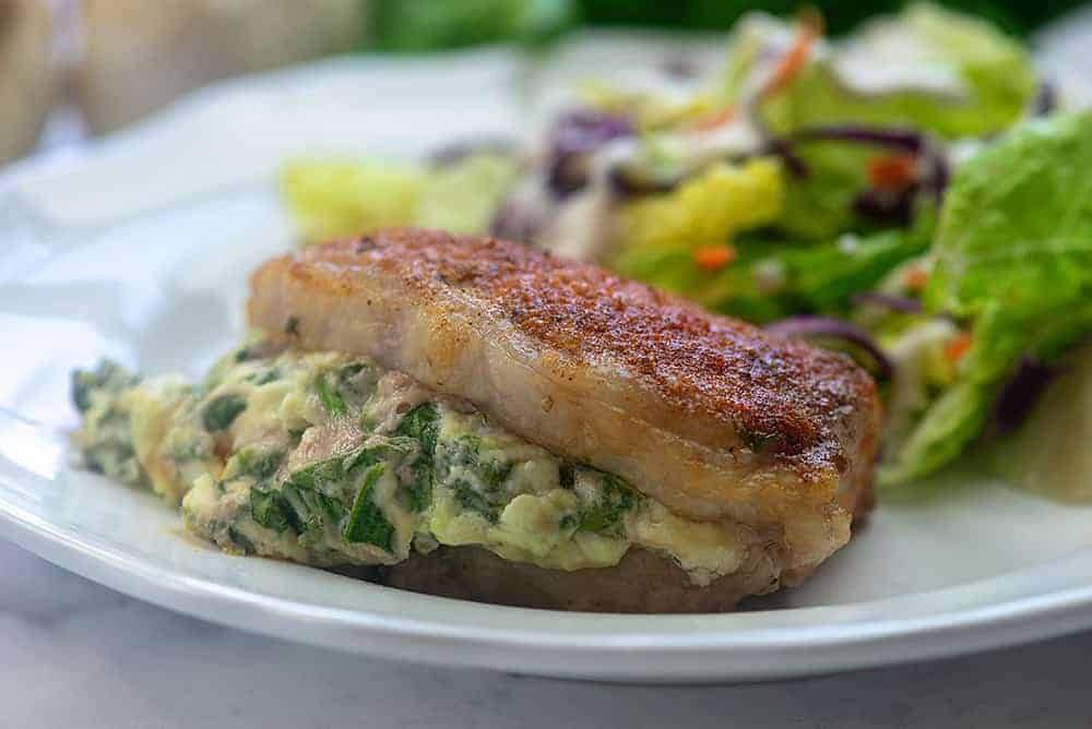 Cooked spinach stuffed pork chops on a white plate.