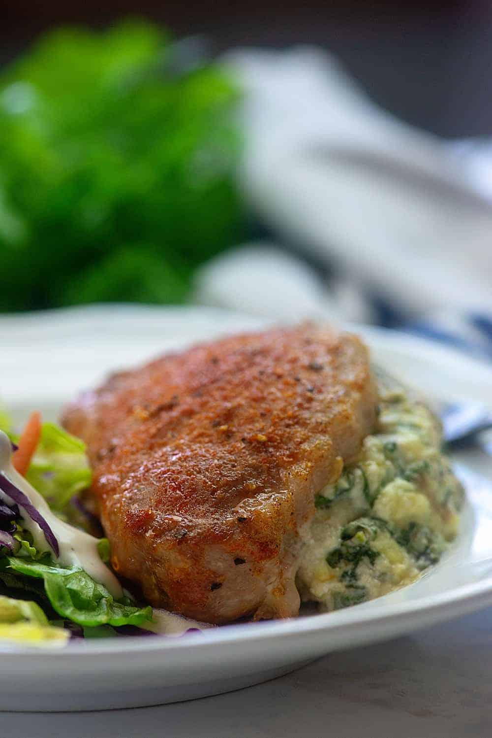 Spinach stuffed pork chop and a salad on white plate.