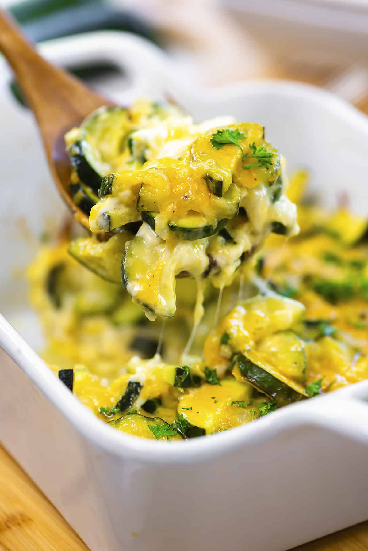 Cheesy zucchini casserole on wooden spoon.