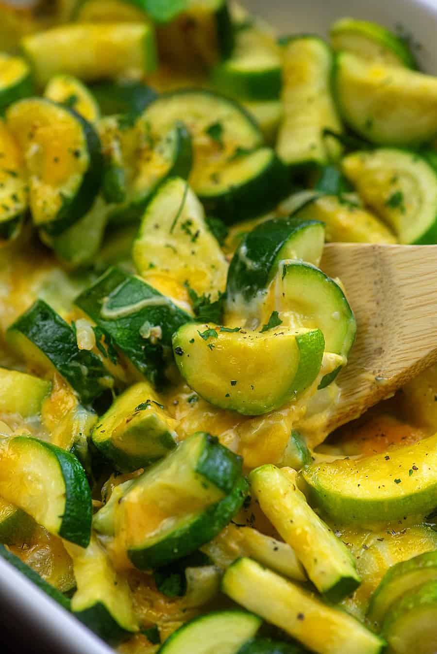 wooden spoon scooping out zucchinis from a baking pan