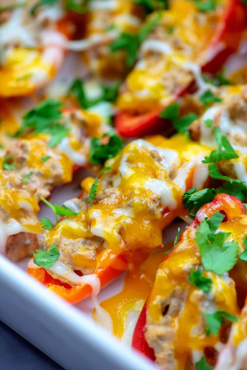 white baking pan with cheese covered peppers in it