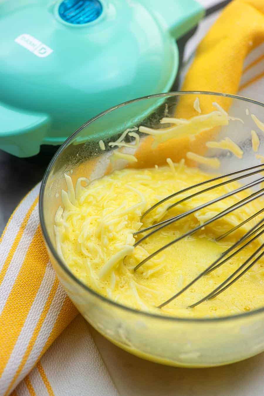 raw egg and cheese being whisked in a glass bowl