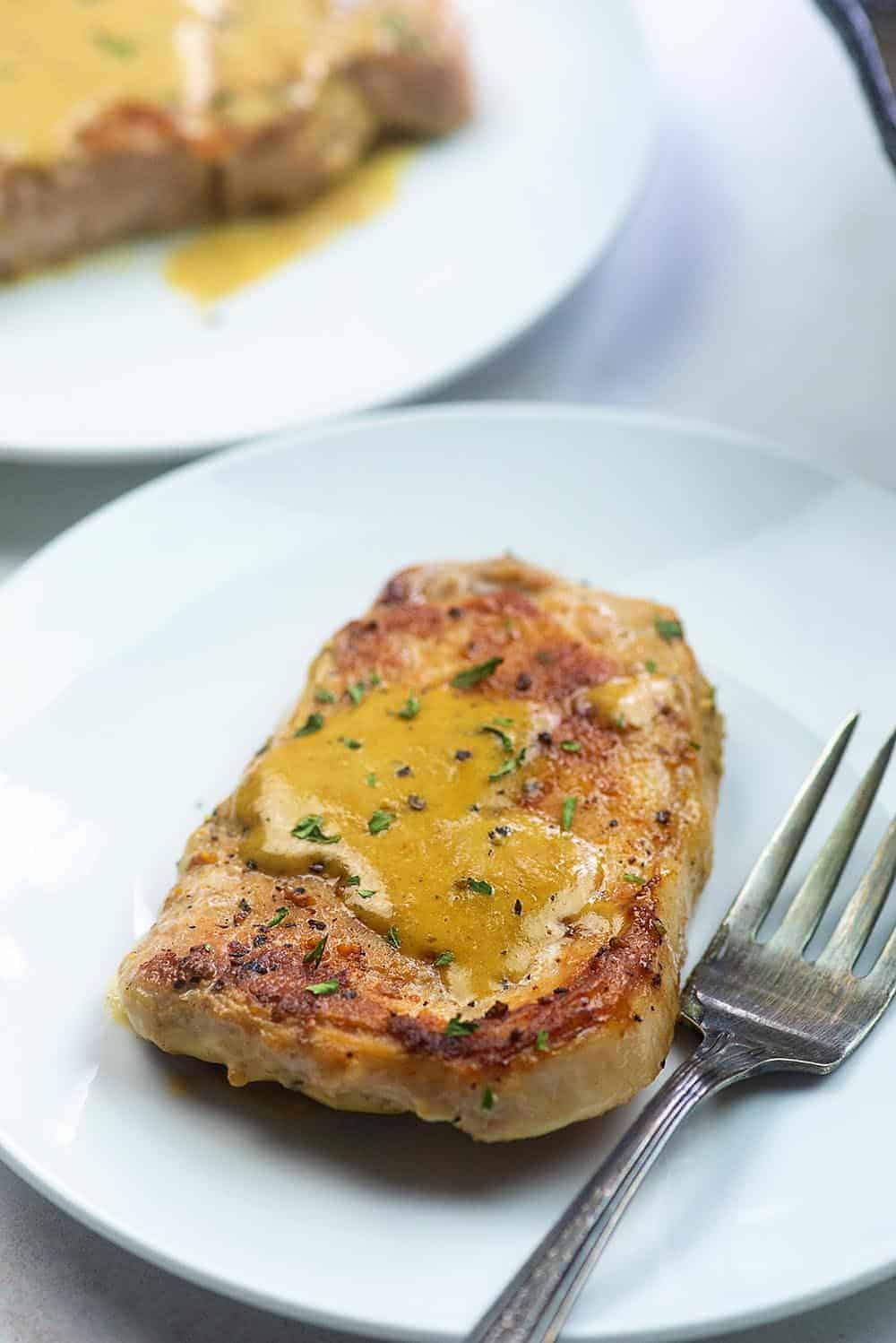 pork chop covered in creamy Dijon sauce on a white plate