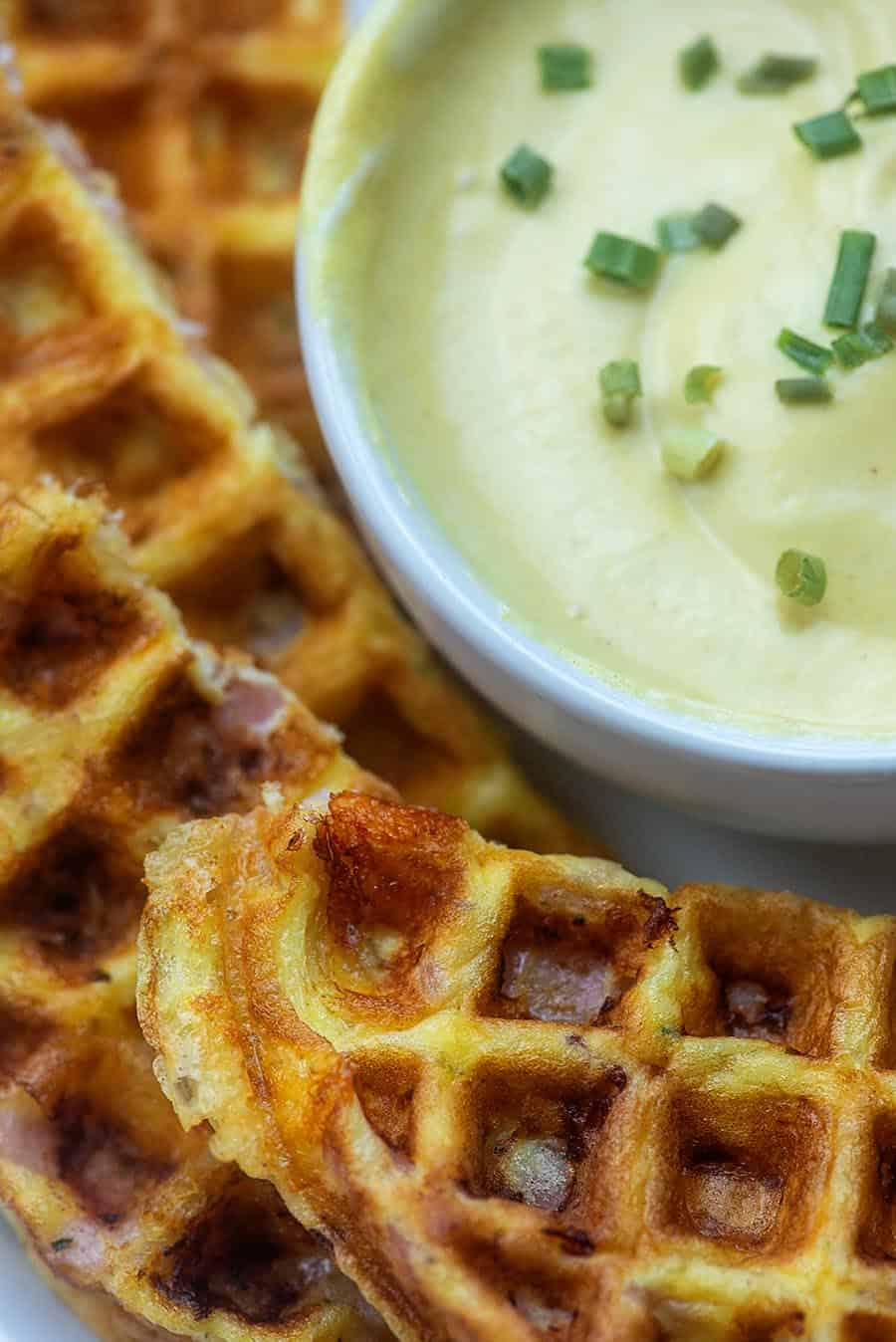A close up of chaffles next to a white cup of cheese dip