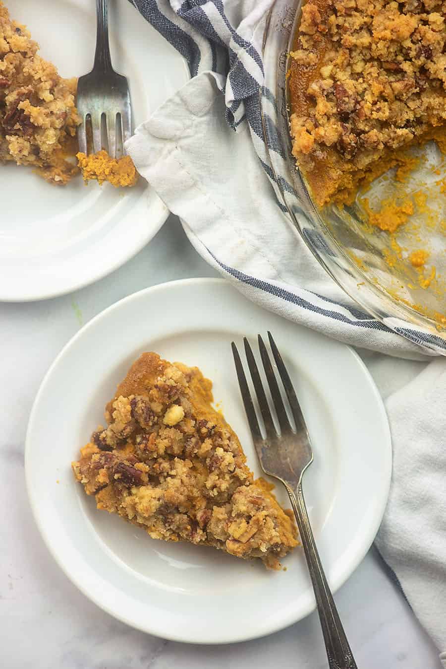 A plate of pumpkin pie next to a pie pan with pumpkin pie in it.