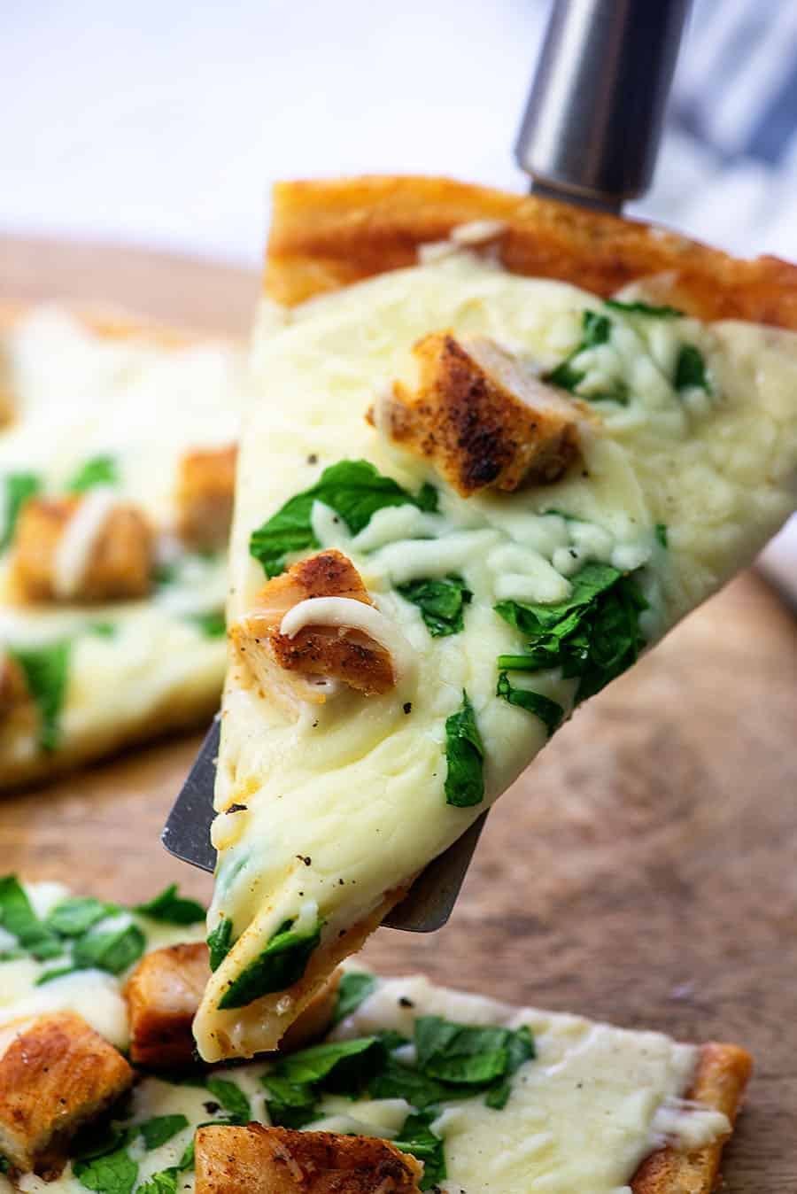 A close up of a slice of chicken pizza being held up to the camera