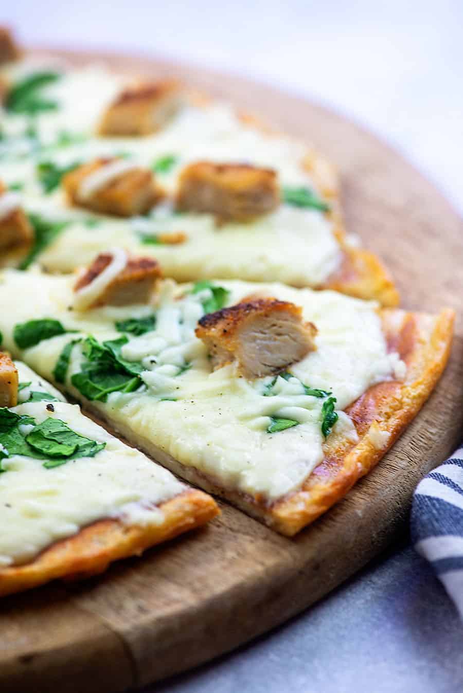 chicken alfredo pizza cut into triangle pieces on a wooden pizza plate