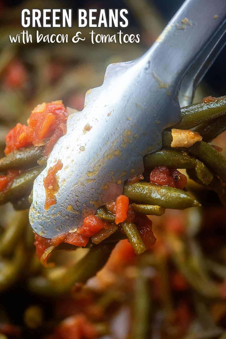 A close up of tongs holding up a bunch of cooked green beans.