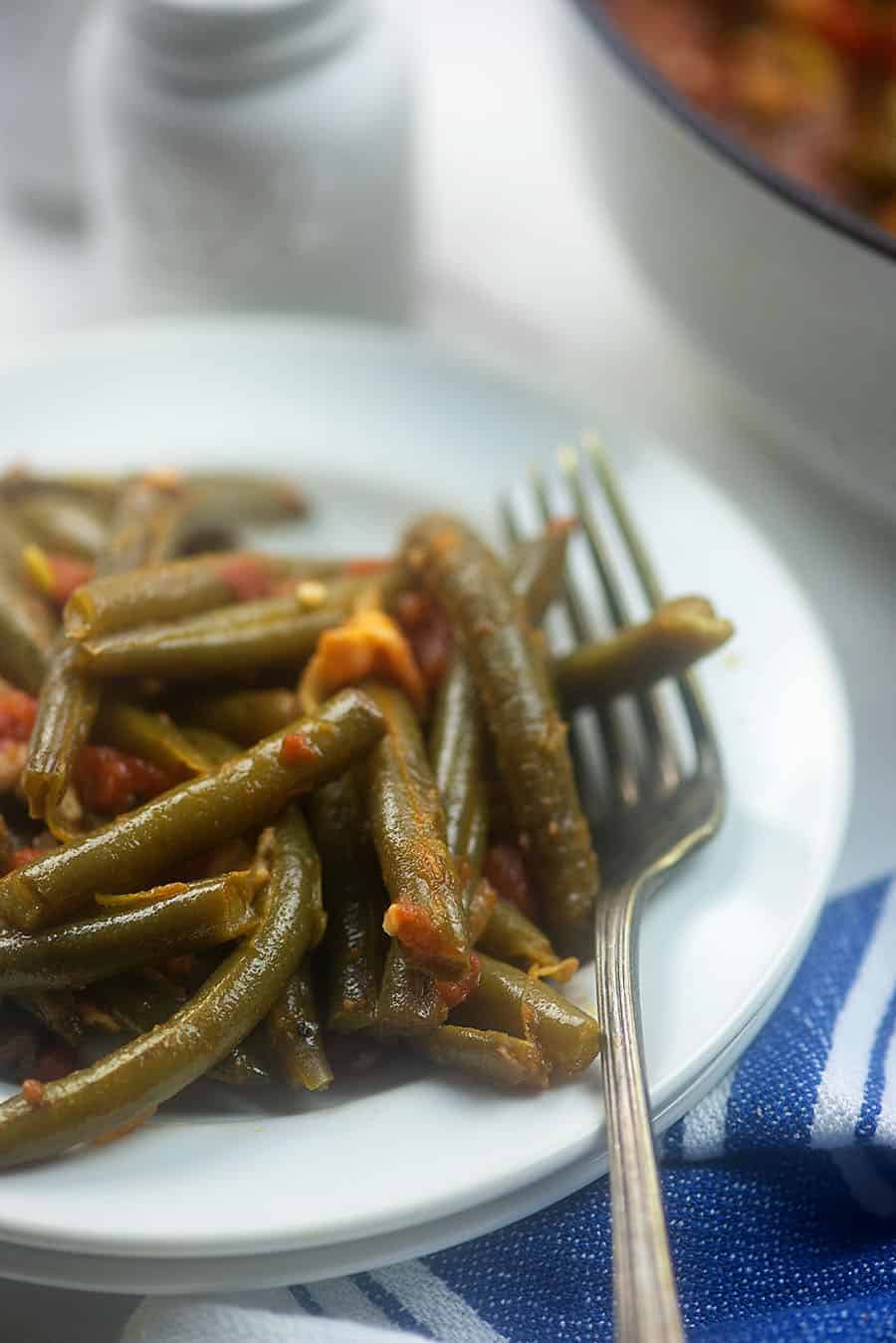 A close up of green beans and a fork on a white plate.