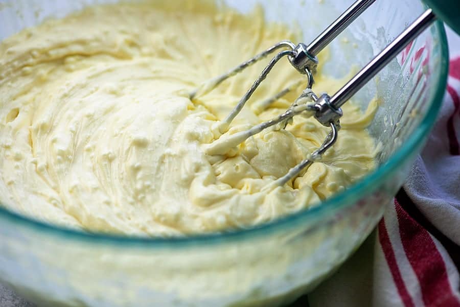 A close up of a beater in a glass bowl of cheesecake batter
