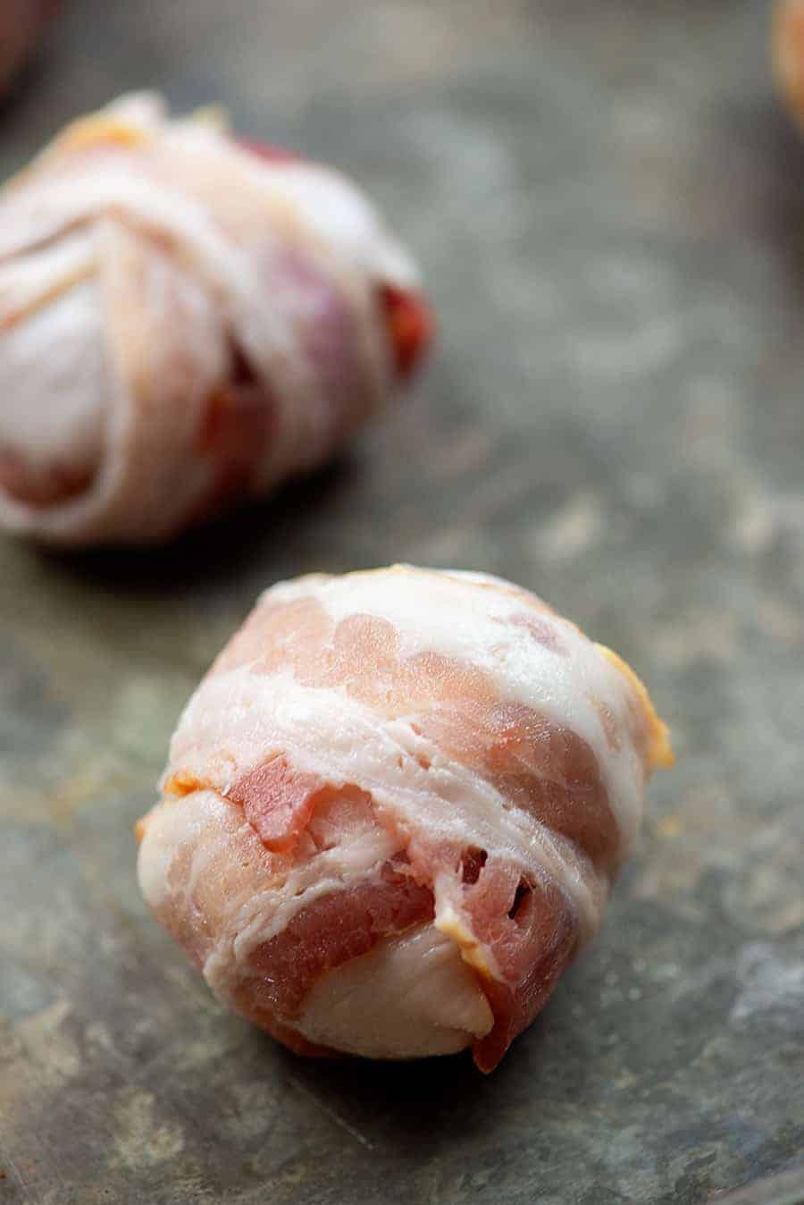 raw bacon wrapped meatballs on a baking sheet