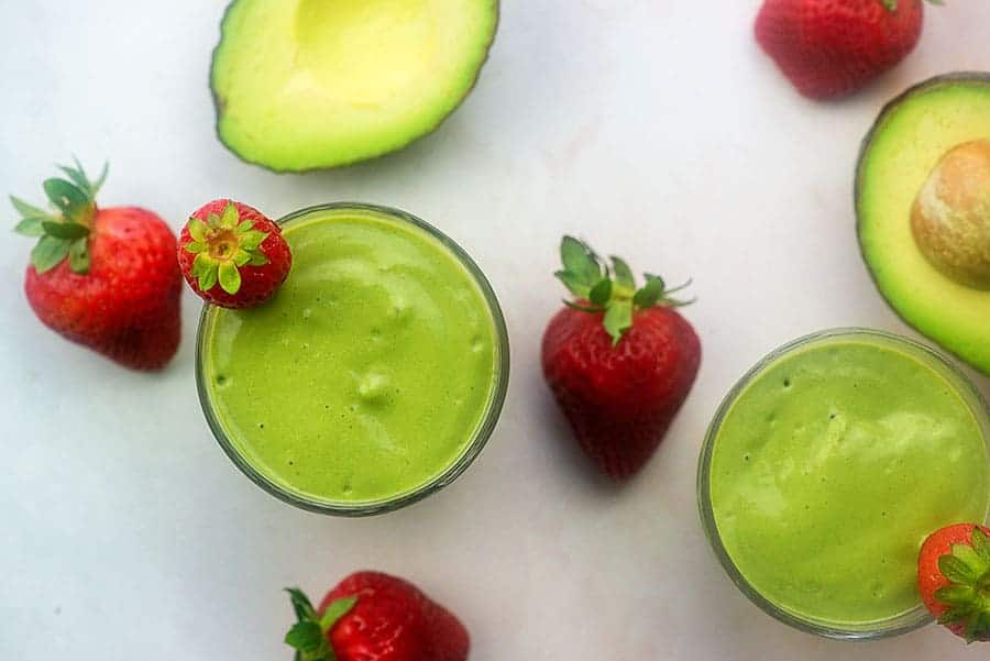 avocado smoothies on a counter with avocados and strawberries