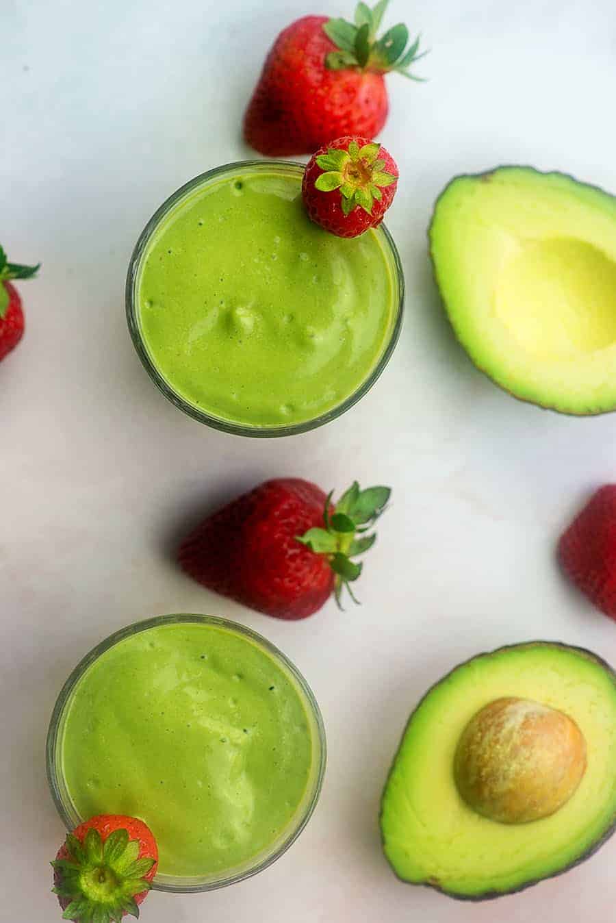 green smoothie with strawberries next to avocados