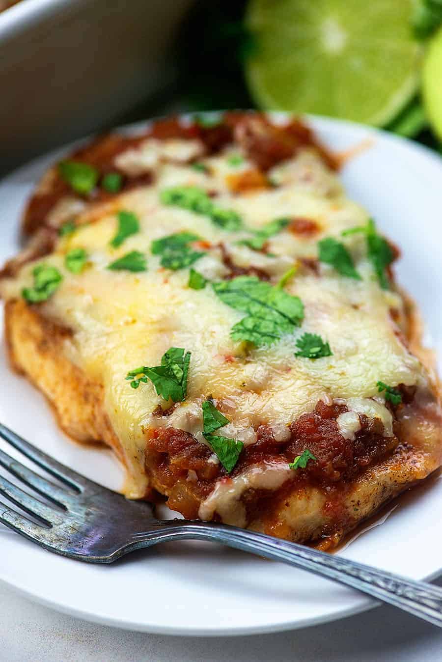 cheesy salso chicken on a white plate with an old fork