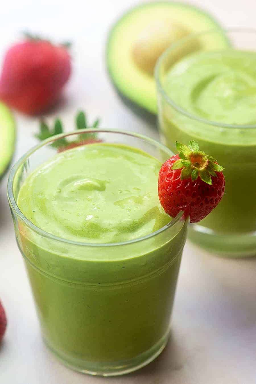 strawberry avocado smoothie in glass with a strawberry on the rim