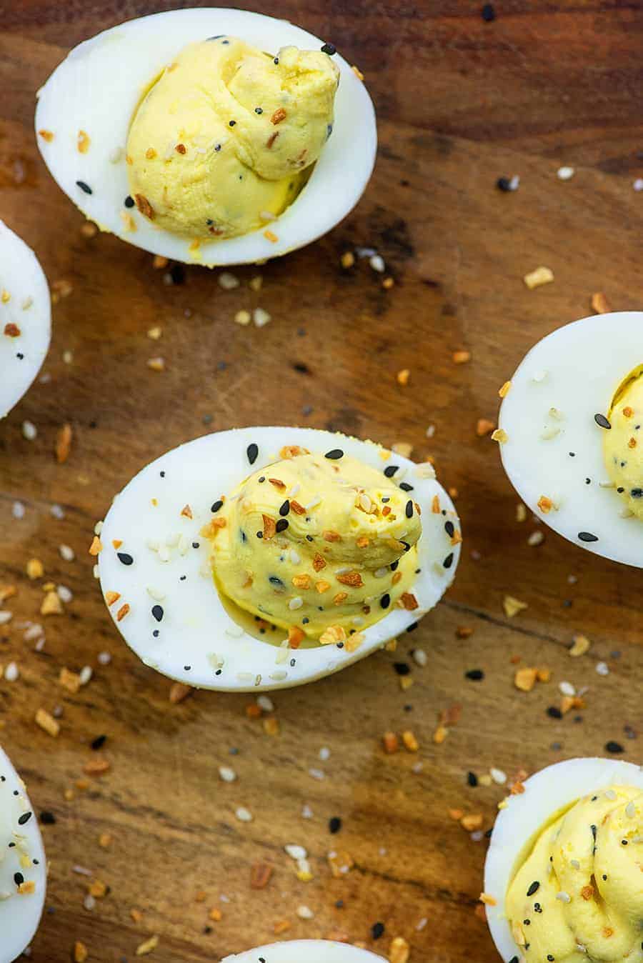 An overhead view of deviled eggs on a wooden cutting board topped with everything bagel seasoning.