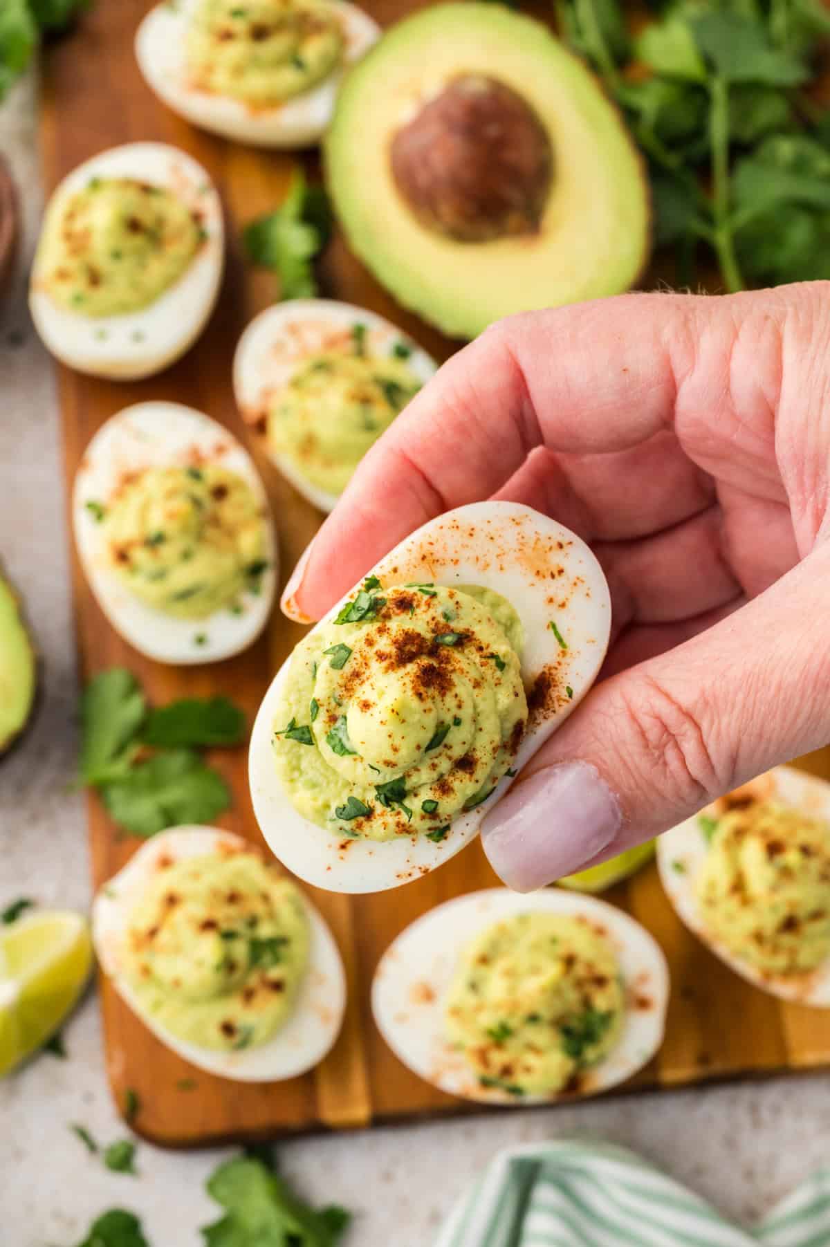 Woman's hand holding an avocado devilled egg.