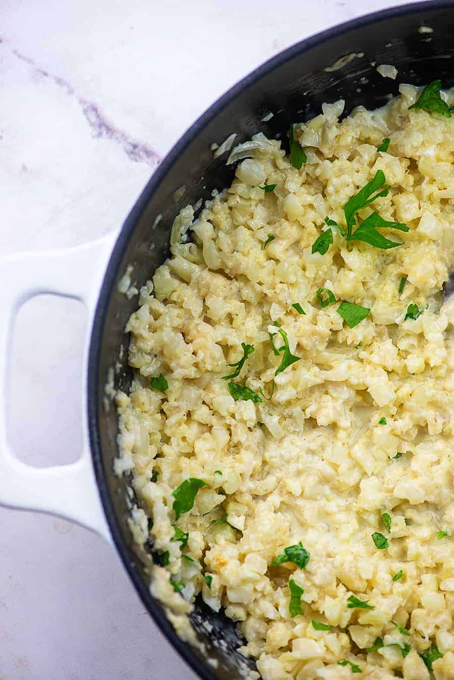 An overhead view of cauliflower risotto in a white cast iron skillet.