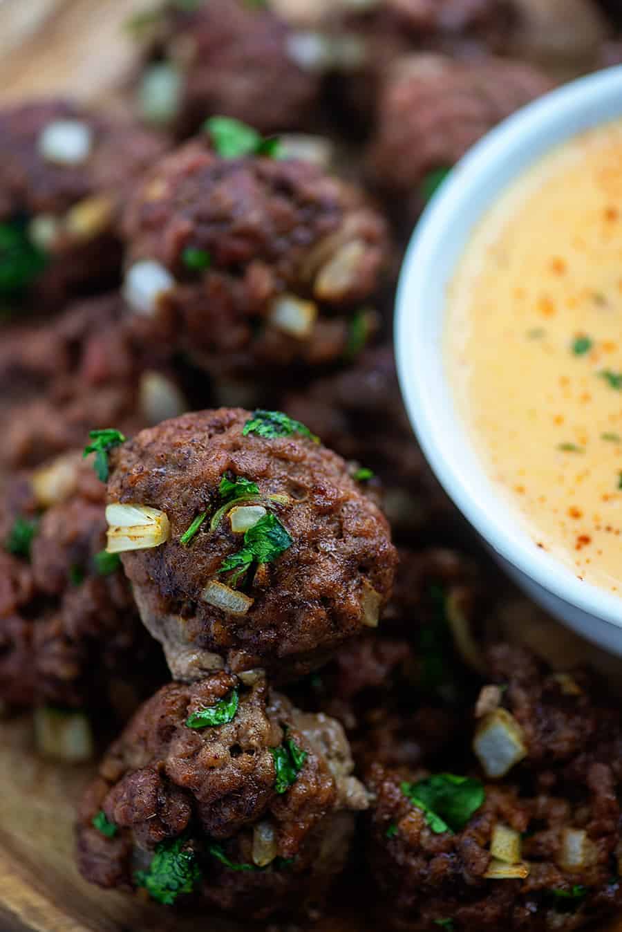 A close up of a bowl of queso dip next to meatballs