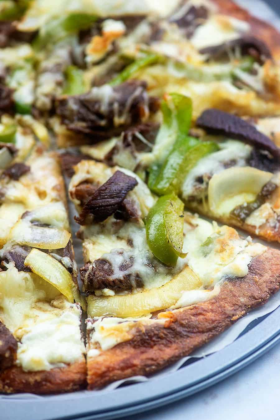 A close up of a Philly cheesesteak pizza cut into triangle pieces.
