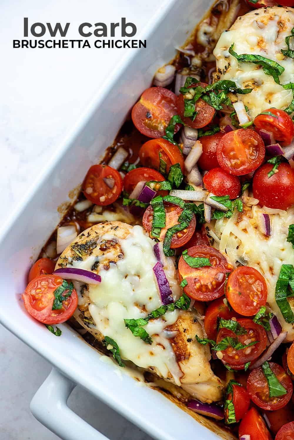 A white baking dish with cheesy chicken and tomatoes in it.