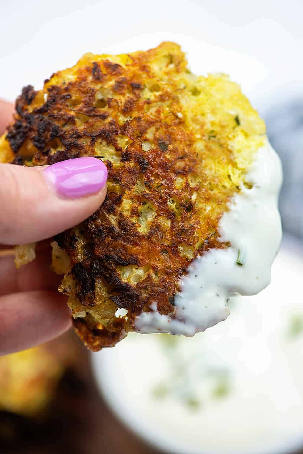 A woman holding up a cauliflower fritter that was dipped in ranch