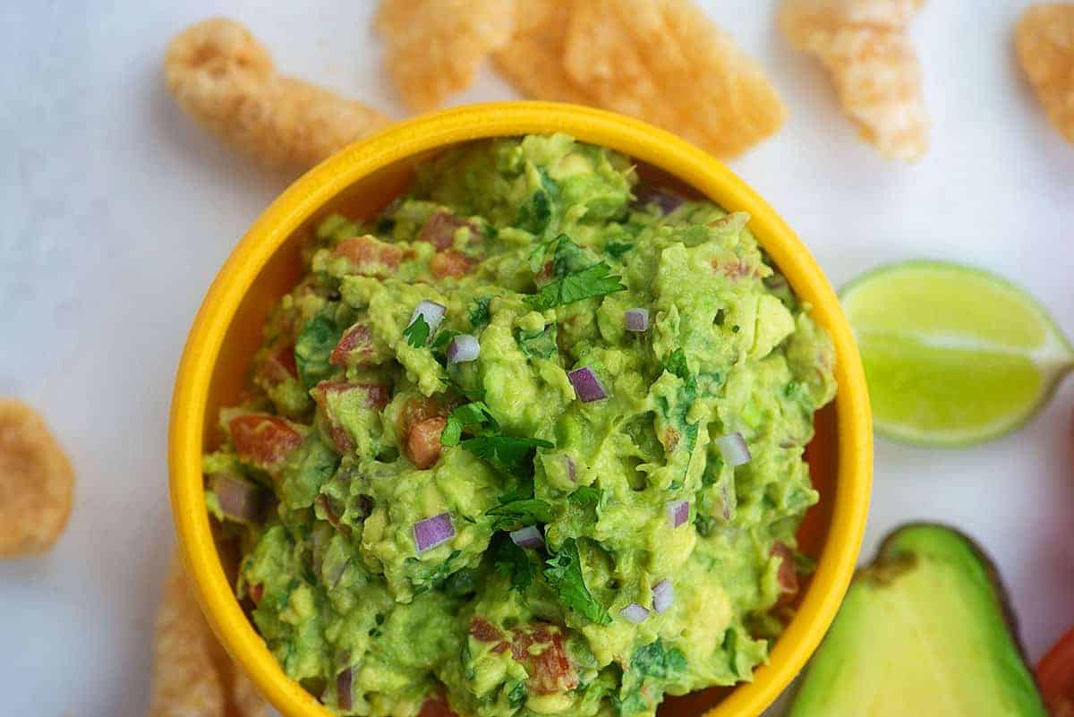 homemade guacamole in yellow bowl with pork rinds