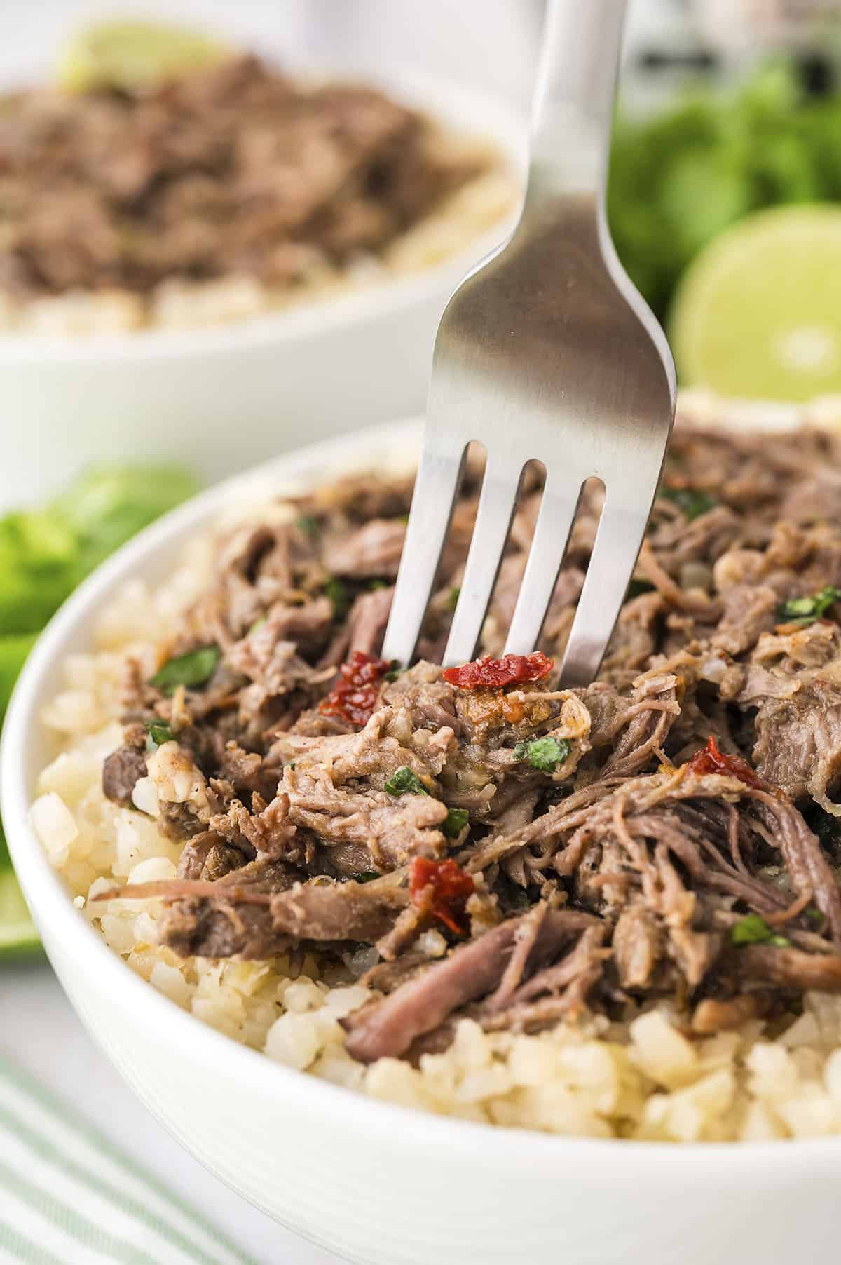 Fork in bowl full of cauliflower rice and Mexican shredded beef.