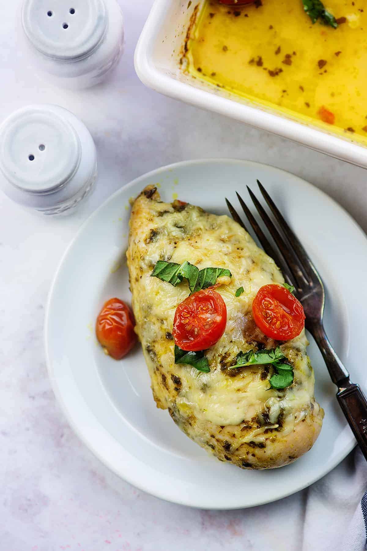 cheesy chicken pesto with cherry tomatoes on white plate