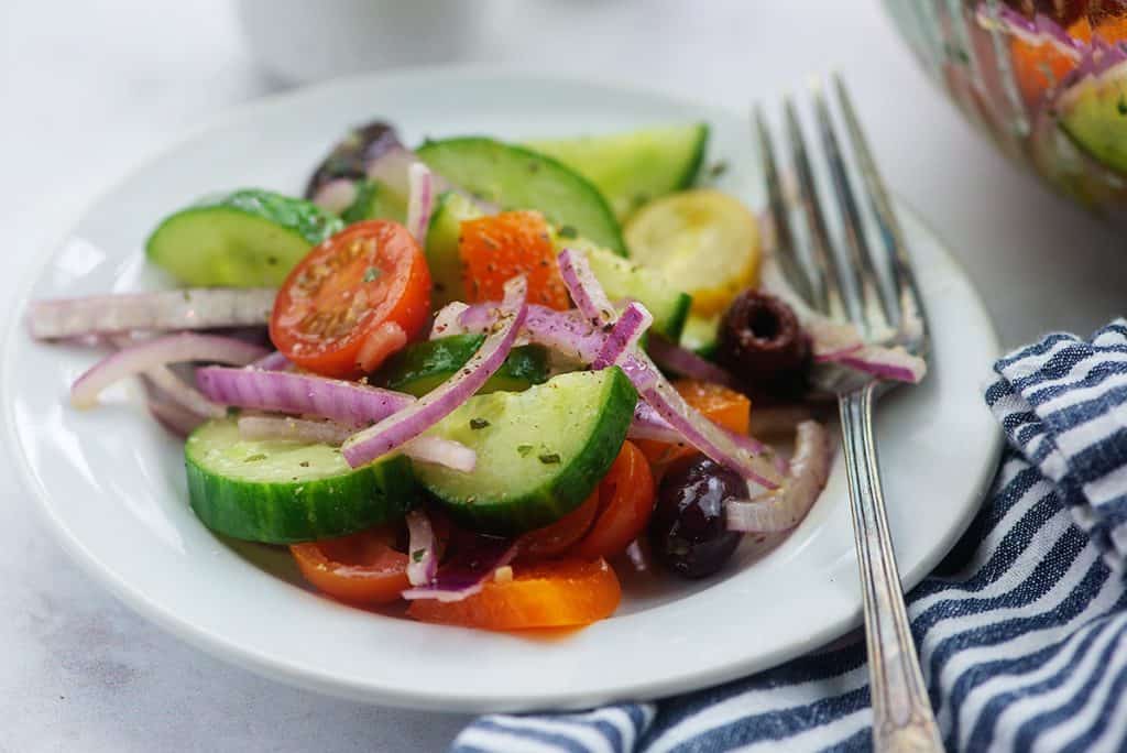 cucumber tomato salad on white plate with vintage fork