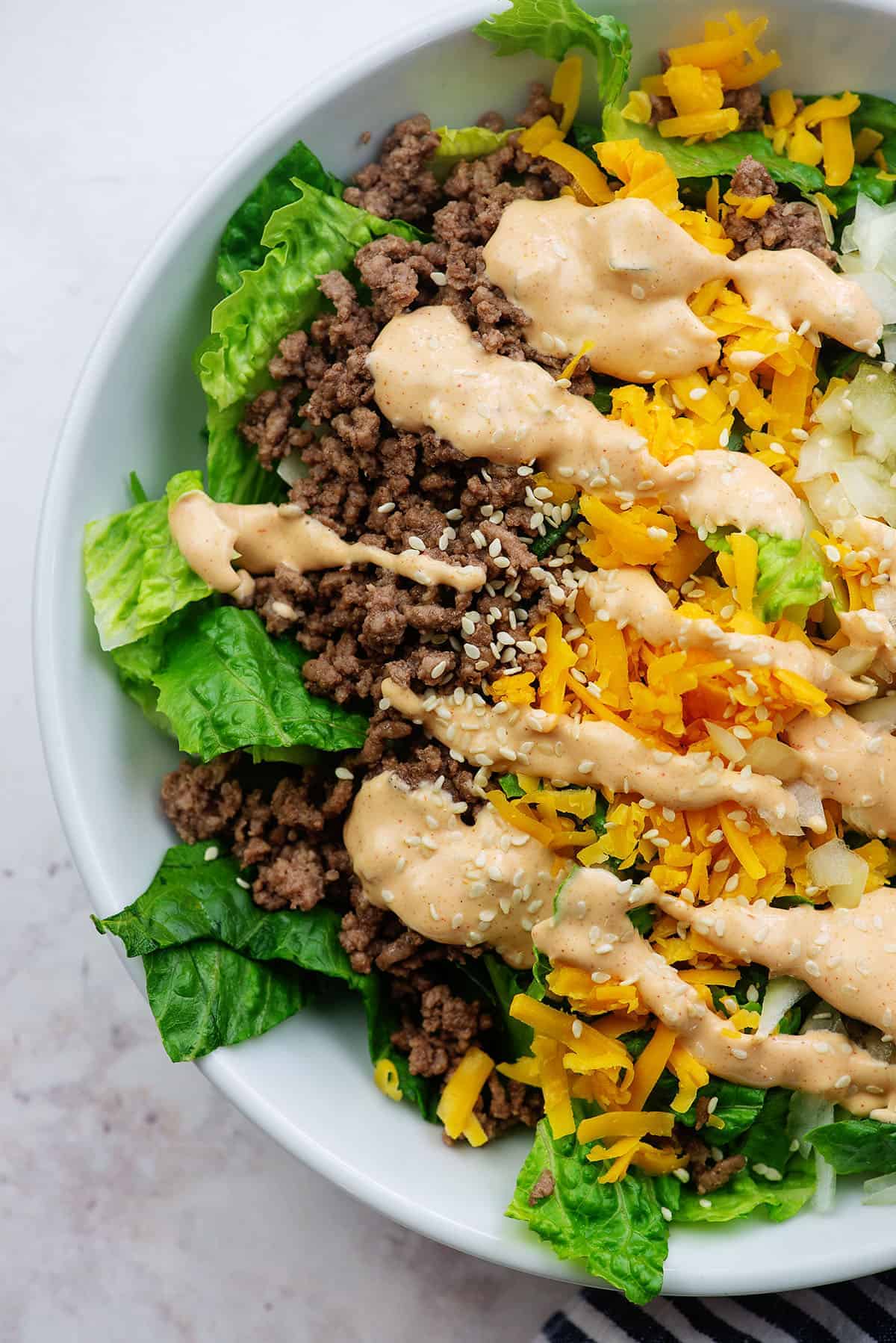 keto salad recipe with ground beef, cheese, pickles, and onions in white bowl