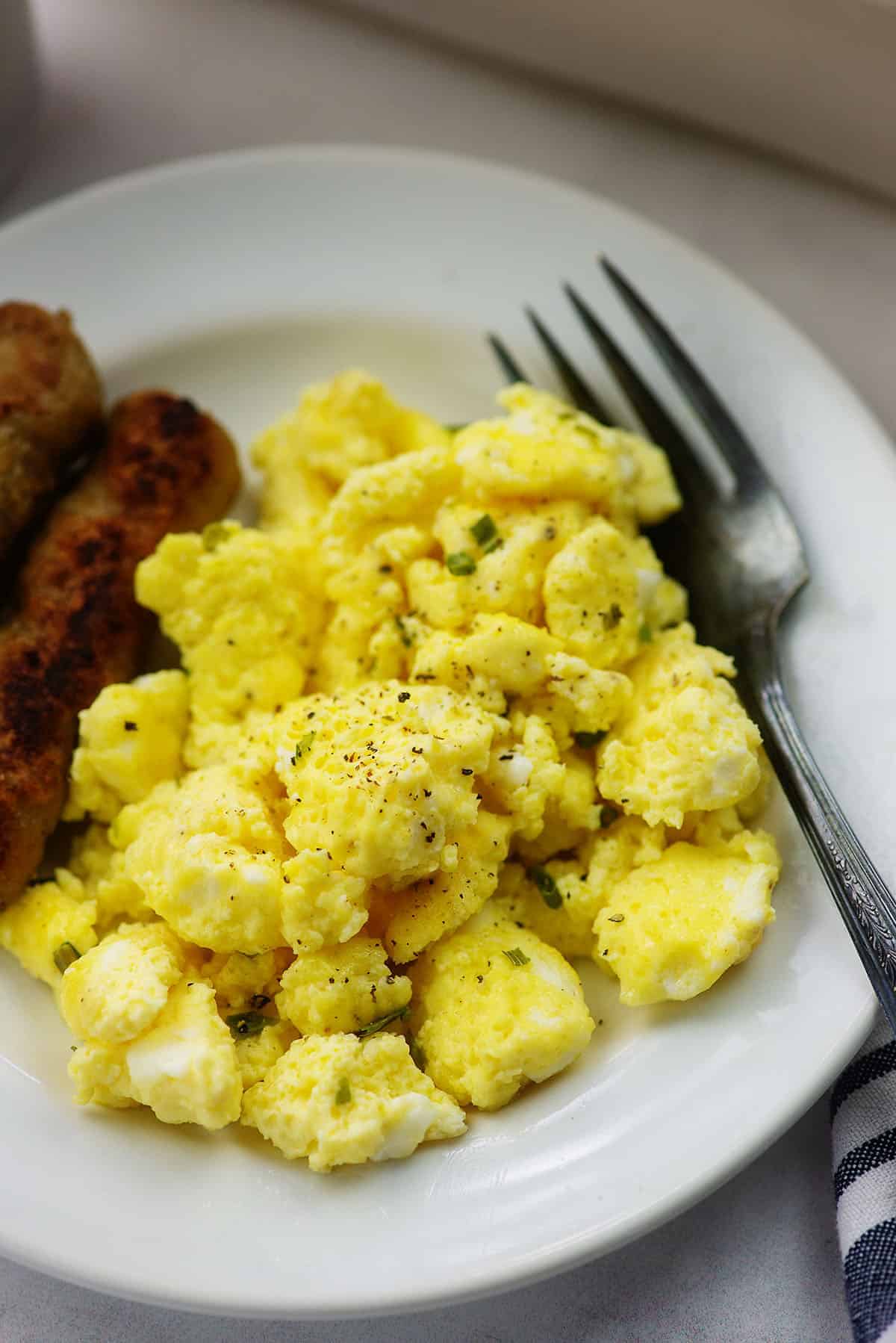 fluffy scrambled eggs on white plate with sausage links