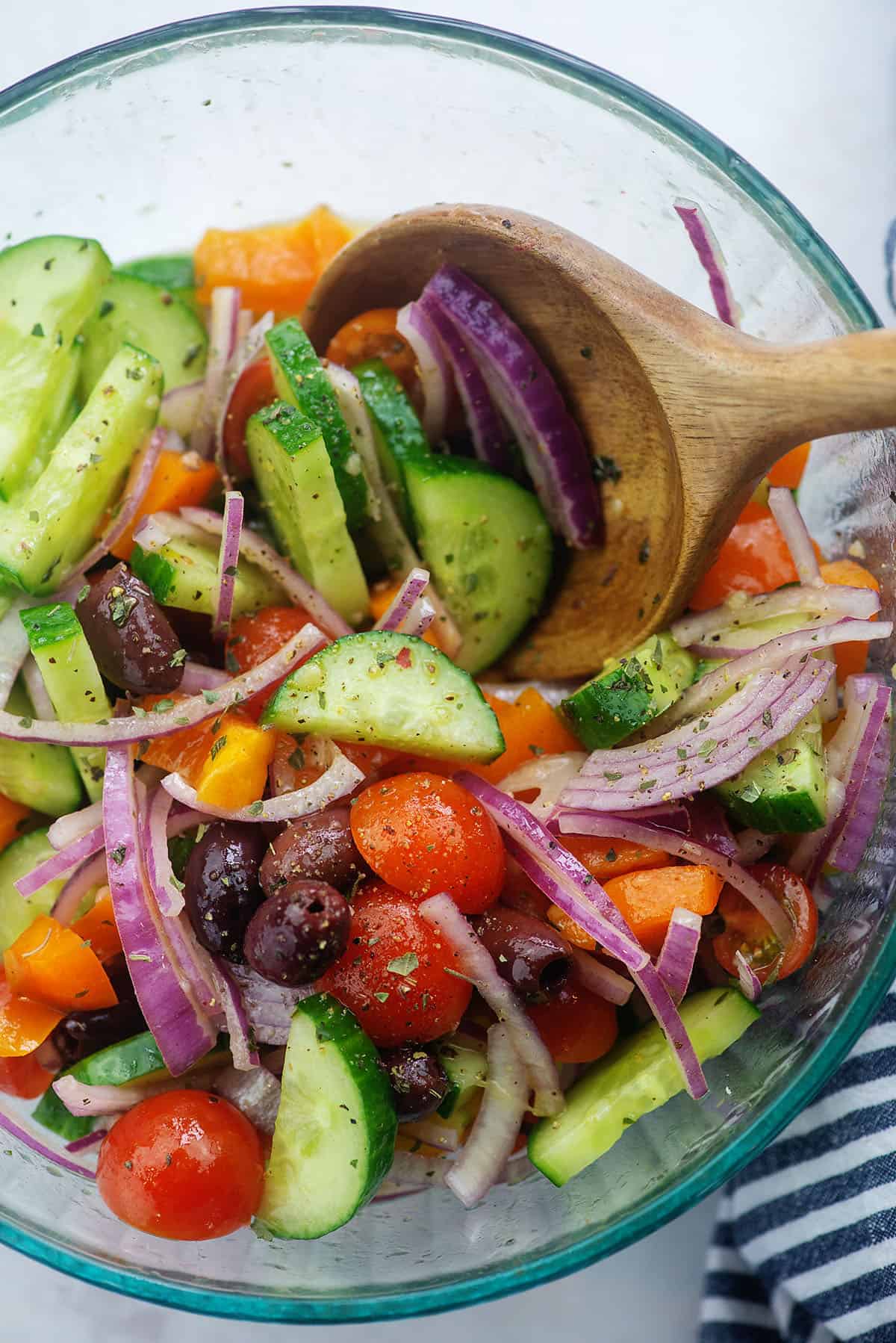 cucumbers, tomatoes, onions, and olives in glass mixing bowl