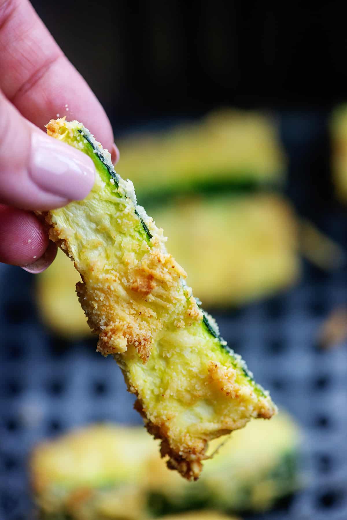 crispy zucchini fry held up over air fryer basket