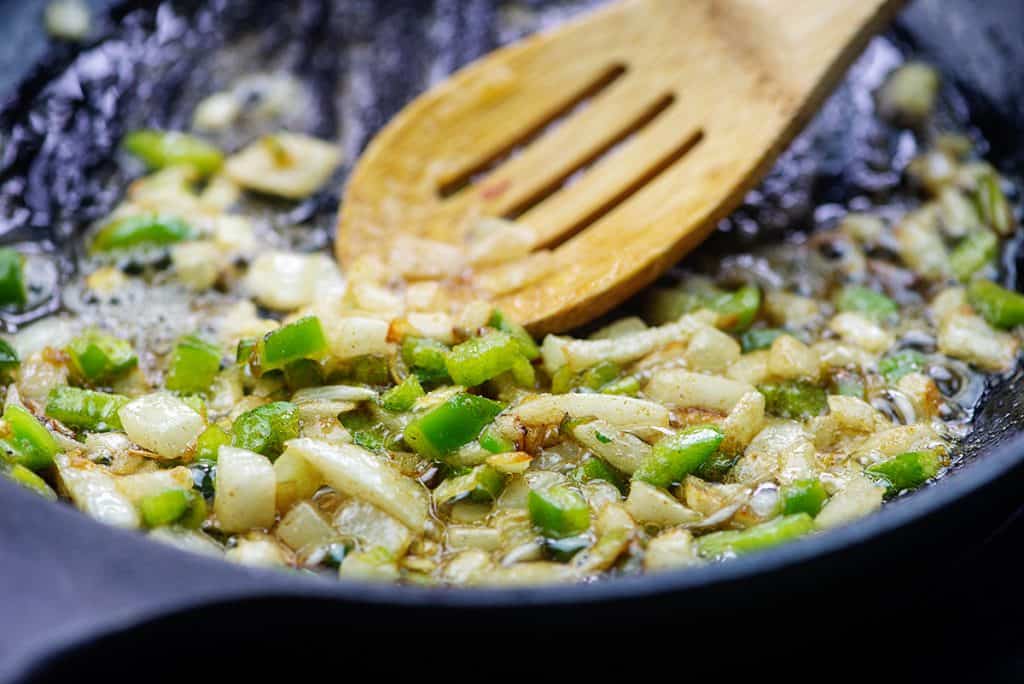onion and jalapenos in cast iron skillet with wooden spoon