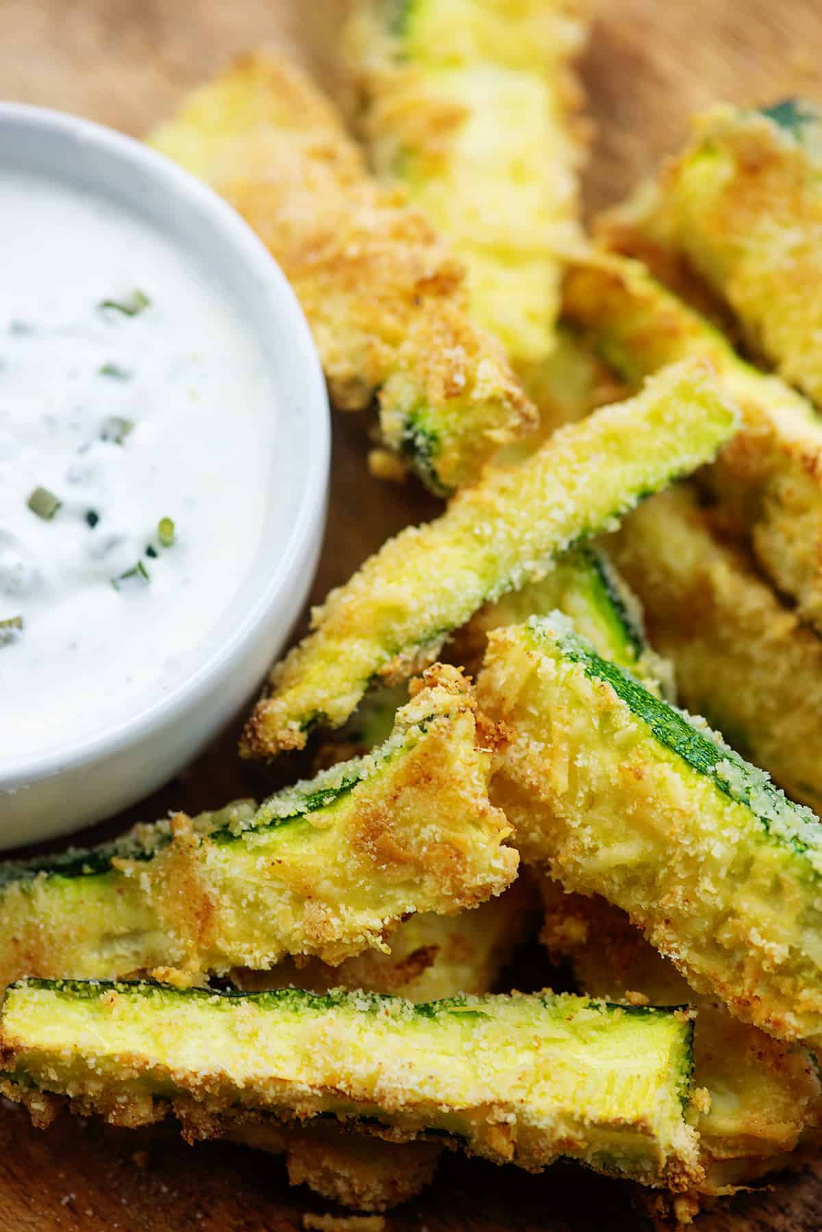 fried zucchini strips on wooden cutting board with ranch dressing